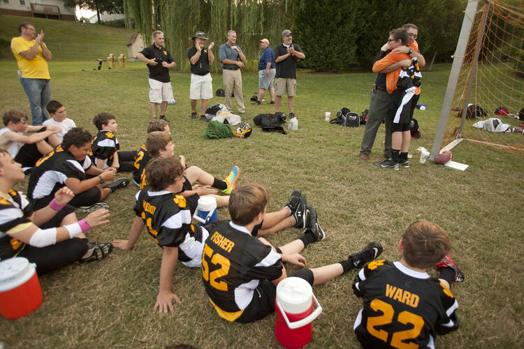 A father embraces his son after handing his son the same number jersey he wore when he played football at St. Henry School in Nashville, Tenn. (CNS photo/Rick Musacchio, Tennessee Register)