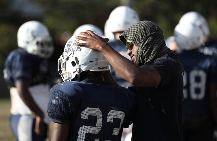 Coach adjusts chin strap on player's football helmet during practice at Maryland Catholic high school.