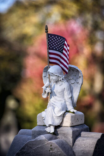 American flag sits on gravestone topped by angel figure at Wisconsin cemetery. (CNS photo/Sam Lucero, The Compass) 