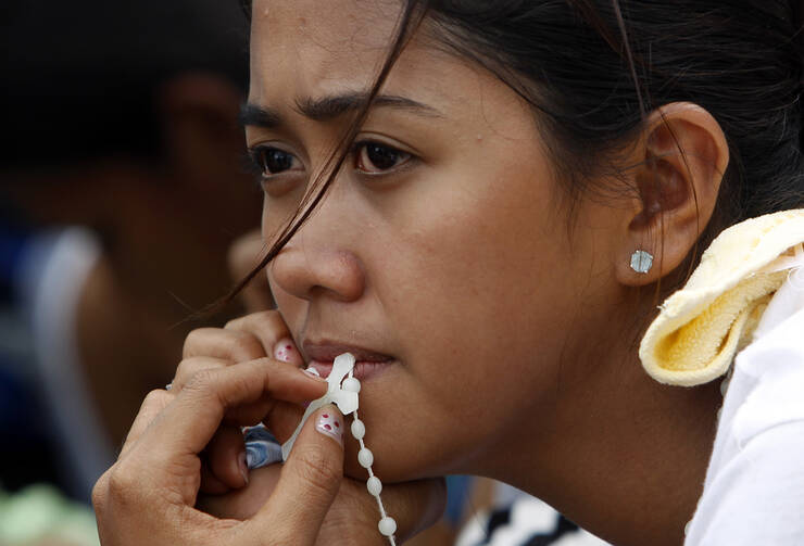 Woman with rosary waits for evacuation flight from tyhoon-battered city in Philippines (CNS photo/Edgar Su, Reuters)