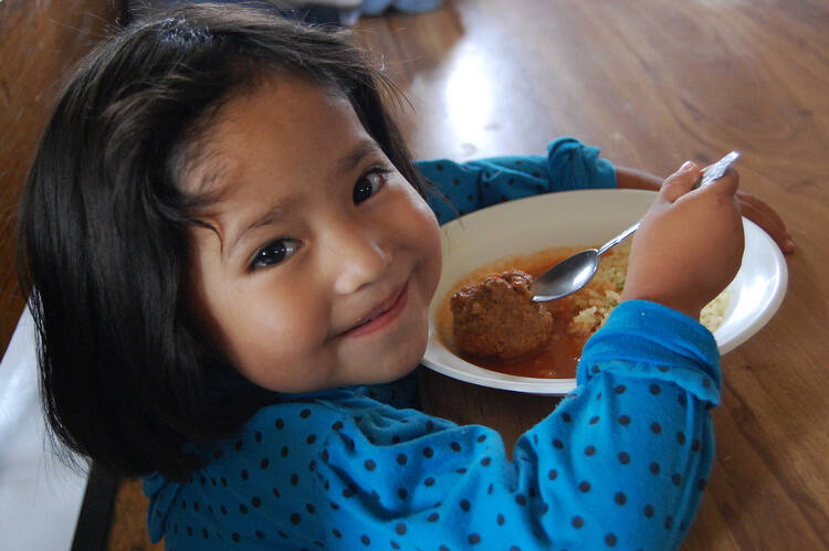 Girl eats meal provided by charity, local Caritas program in Mexico.