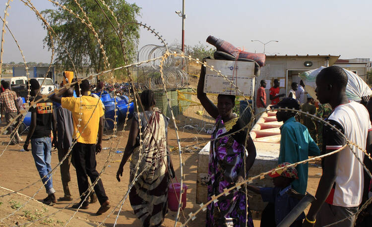 People walk past razor wire Jan. 7 at Tomping camp, where thousands of displaced people who fled their homes are sheltered by the United Nations near Juba, South Sudan. (CNS photo/James Akena, Reuters)