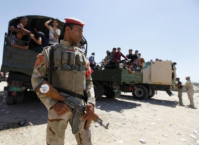 Member of Iraqi security forces stands guard in front of army volunteers. (CNS photo/Ahmed Saad, Reuters)