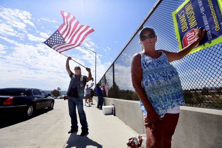 Protesters against illegal immigration hold signs and wave flags to motorists on highway overpass. (CNS photo/Sandy Huffaker, Reuters)
