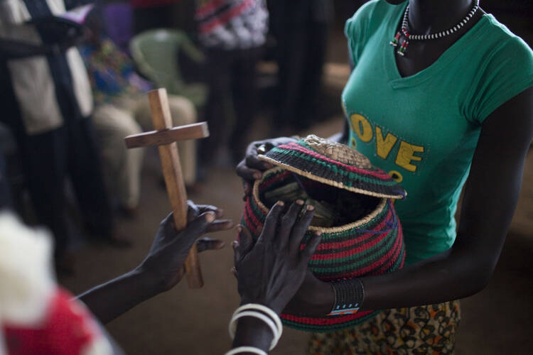 South Sudanese woman gives alms during Mass in camp for displaced people. (CNS photo/Jim Lopez, EPA)