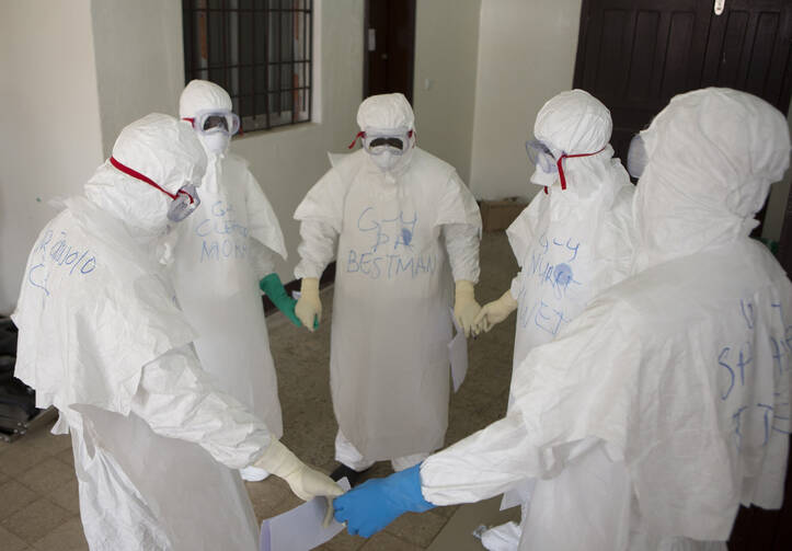 Health workers wearing protective equipment hold hands as they pray at the start of their shift before entering the Ebola treatment center in Monrovia, Liberia, Sept.30. Joe Sehnert, a member of Ascension Parish in Chesterfield, Mo., is helping the local community cope with the Ebola outbreak as a lay missionary with Liberia Mission, an effort of Franciscan Works. (CNS photo/Christopher Black, WHO, Handout via Reuters) See EBOLA-SEHNERT Oct. 8, 2014.