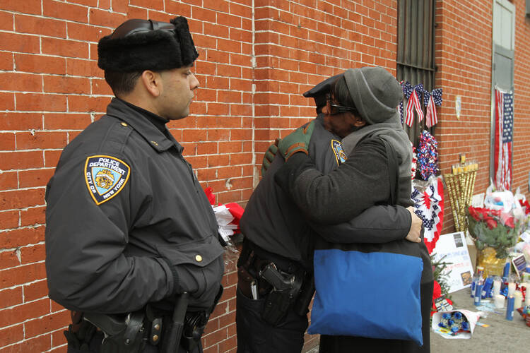 A woman hugs a New York Police Department officer Dec. 22 next to a makeshift memorial near the site where two police officers were assassinated in their patrol car Dec. 20 in the Brooklyn borough of New York. Police said Ismaaiyl Brinsley allegedly ambu shed officers Rafael Ramos and Wenjian Liu, fatally shooting them before committing suicide inside a subway station. (CNS photo/Gregory A. Shemitz) See NYPD-MURDERED Dec. 22, 2014.