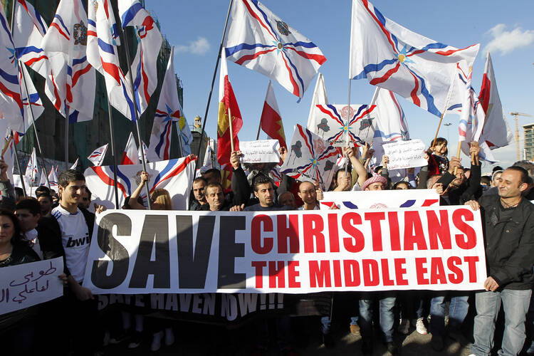 Assyrian Christians, who had fled Syria and Iraq, carry placards and wave Assyrian flags during a gathering in late May in front of U.N. headquarters in Beirut. (CNS photo/Nabil Mounzer, EPA)