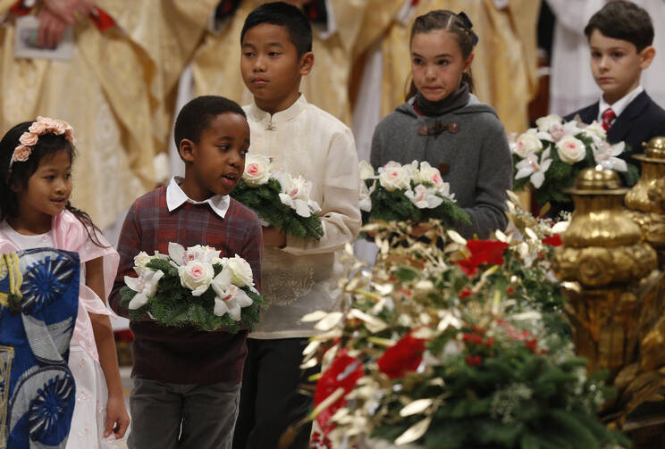 Children carry flowers to place at a figurine of the baby Jesus as Pope Francis celebrates Christmas Eve Mass in St. Peter's Basilica at the Vatican on Dec. 24. (CNS photo/Paul Haring)