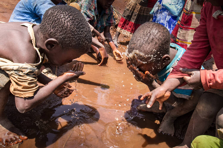Refugee children wash their faces in a puddle in the refugee camp at Mwanza, Malawi, Feb. 8. (CNS photo/Erico Waga, EPA) 