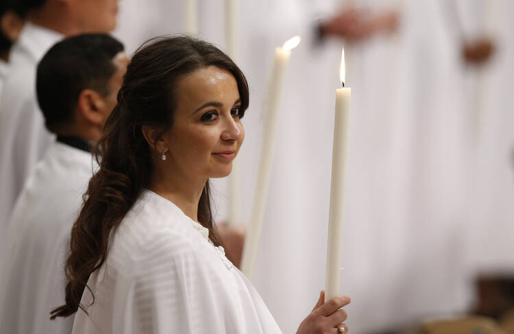 A new member of the church holds a candle as Pope Francis celebrates the Easter Vigil in St. Peter's Basilica at the Vatican March 26. The pope baptized 12 people at the vigil. (CNS photo/Paul Haring)