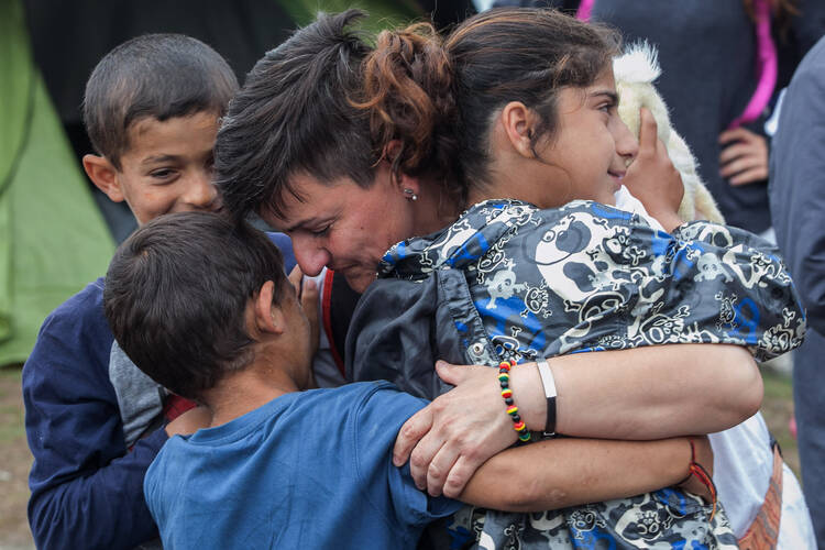 A volunteer from a humanitarian organization hugs refugee children June 13 during a police operation at a makeshift camp in Polykastro, Greece. (CNS photo/Nikos Arvantidis, pool via EPA)