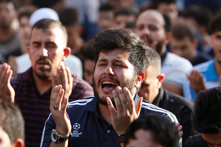 Muslim men pray on July 6 at the site of a July 3 suicide car bomb attack at a shopping area in Baghdad. (CNS photo/Khalid-Mousily, Reuters)