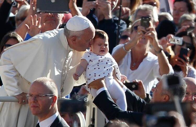 Pope Francis kisses a crying baby during his general audience in St. Peter's Square at the Vatican on Oct. 5. (CNS photo/Paul Haring)