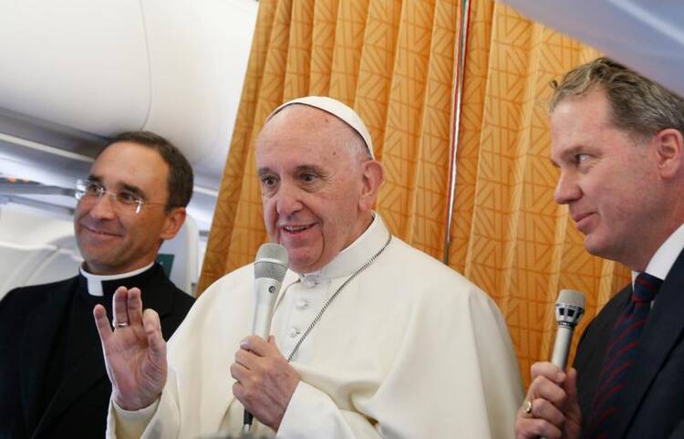 Pope Francis answers questions from journalists aboard his flight from Malmo, Sweden, to Rome Nov. 1. At left is Father Mauricio Rueda Beltz, papal trip planner; at right is Greg Burke, Vatican spokesman.(CNS photo/Paul Haring)