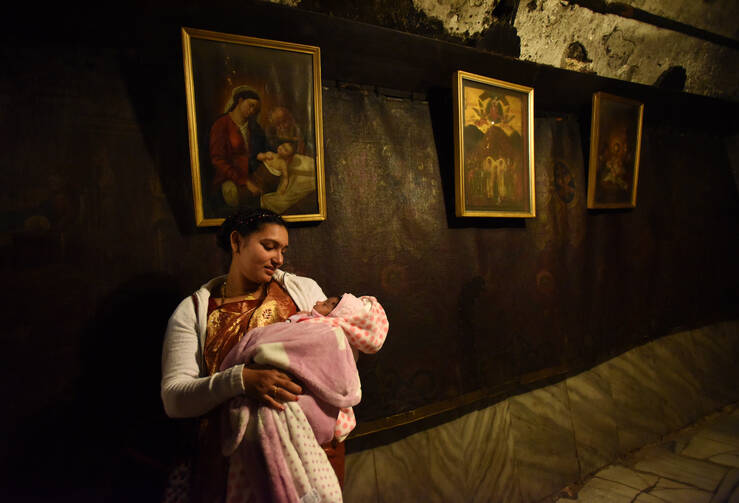 A pilgrim from India holds her baby in front of a painting of the Mary and the Christ Child in the grotto of the Church of Nativity in Bethlehem. (CNS photo/Debbie Hill)