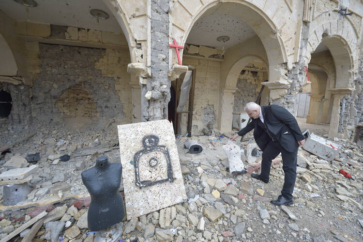 Father Emanuel Youkhana, an archimandrite of the Assyrian Church of the East, looks through the rubble of a Syriac Catholic Church on Jan. 27 in Qaraqosh, Iraq. The mannequin and poster were used as target practice. (CNS photo/Paul Jeffrey)