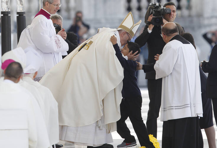 Pope Francis embraces Lucas Batista from Brazil as offertory gifts are presented during the canonization Mass of Sts. Francisco and Jacinta Marto.