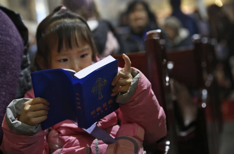 A girl looks at a Bible during Mass in 2016 at a Beijing cathedral. As young people move to cities, Catholic grandparents in rural areas are passing on the faith to their grandchildren. (CNS photo/How Hwee Young, EPA)