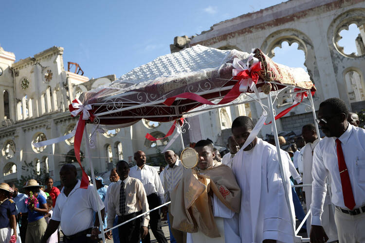 A priest carries a monstrance in a Corpus Christi procession on June 15, 2017, as people pass the ruins of the the Cathedral of Our Lady of the Assumption in Port-au-Prince, Haiti. (CNS photo/Andres Martinez Casares, Reuters)