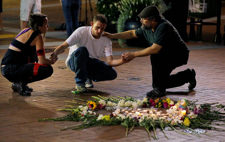 Two people comfort Joseph Culver of Charlottesville, Va., Aug. 12 as he kneels at a late night vigil to pay his respects for a friend injured in a car attack on counter-protesters rallying against white nationalists. (CNS photo/Jim Bourg, Reuters)