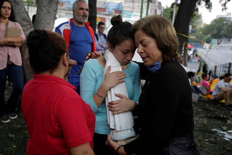 A young woman holding a statue of Mary is comforted by family members of a person trapped in the rubble of a collapsed building on Sept. 26 in Mexico City. Five days after the deadly magnitude 7.1 earthquake, the collapsed seven-story office building is one of the last hopes searchers believe they may still find someone trapped alive. (CNS photo/Jose Luis Gonzalez, Reuters)