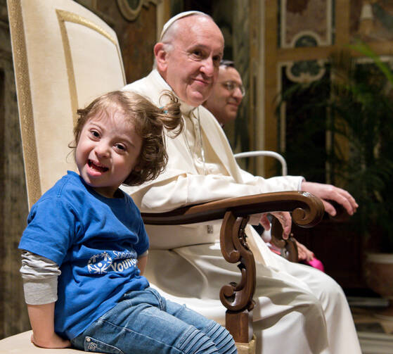 A young girl sitting next to Pope Francis smiles during an audience with Special Olympics athletes participating in the Unified Football tournament, at the Vatican Oct. 13. (CNS photo/L'Osservatore Romano)