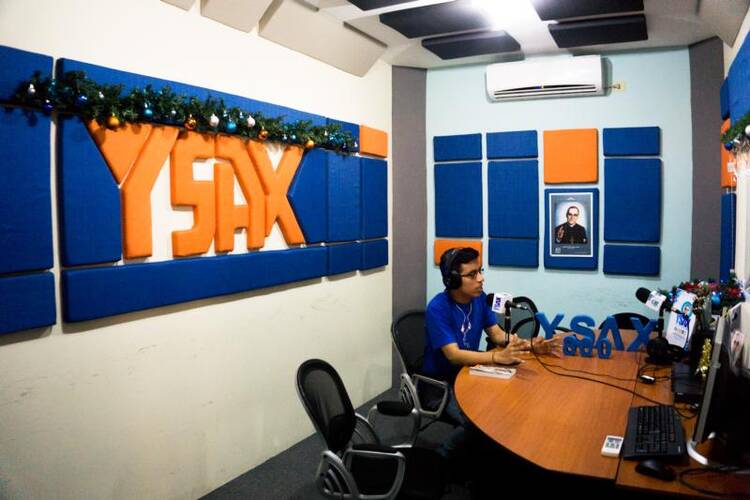 A photo of Blessed Oscar Romero is displayed as a YSAX radio volunteer works in the studio on Dec. 9 in San Salvador, El Salvador. In San Salvador's traffic jams or at work, people turn on radio YSAX to listen to Blessed Romero's homilies, just as they did over 30 years ago. (CNS photo/Melissa Vida) 