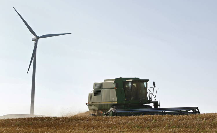 A combine harvests wheat near a wind turbine close to Lincoln, Kan., in this 2008 file photo. Two religious communities were pleased that two Midwest utilities recently agreed to publish climate risk assessment reports in alignment with the Paris climate accord. (CNS photo/Larry W. Smith, EPA) See SHAREHOLDERS-CLIMATE March 2, 2018.