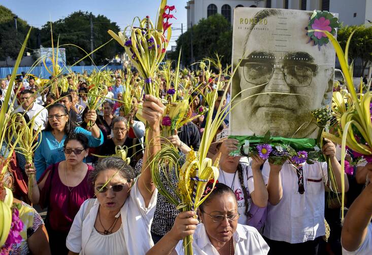 Worshippers wave palm fronds near an image of Blessed Oscar Romero during a Palm Sunday procession March 25 in San Salvador, El Salvador. Catholic officials in El Salvador were shaken and expressed outrage and sadness after the assassination of a 36-year-old priest during Holy Week, in what some suspect may be a gang killing. (CNS photo/Armando Escobar, EPA)