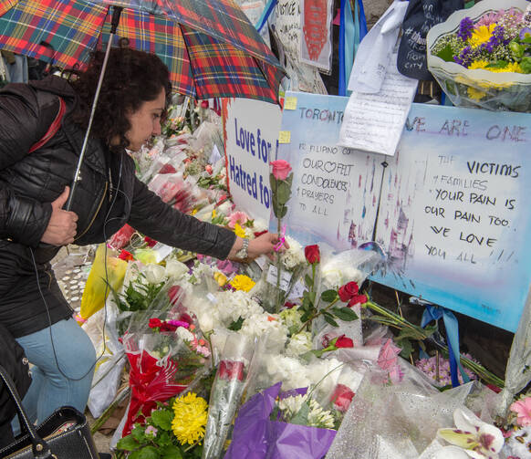 A woman places a flower at a makeshift memorial on April 25 near the Toronto sidewalk where 10 people were killed on April 23 after a van ran into them. (CNS photo/Michael Swan, The Catholic Register)