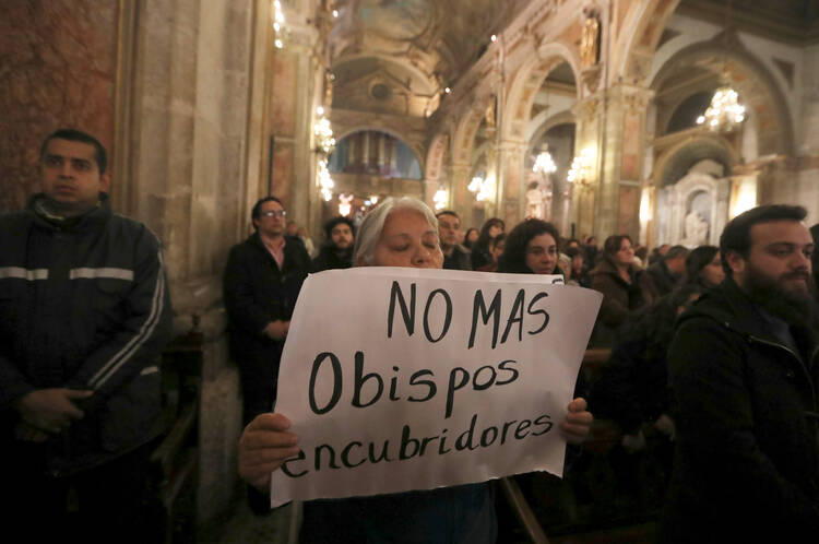 A woman holds a sign in protest while praying as Cardinal Ricardo Ezzati of Santiago, Chile, celebrates Mass on July 25 at the cathedral in Santiago. The Chilean prosecutor's office has issued a subpoena to Cardinal Ezzati regarding his role in the alleged cover-up of sexual abuse by clergy members. (CNS photo/Ivan Alvarado, Reuters) 