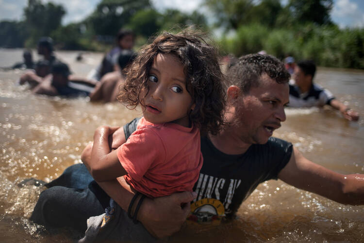 A man, part of a caravan of migrants from Central America to the United States, carries a girl Oct. 29 through the Suchiate River into Mexico from Guatemala. (CNS photo/Adrees Latif, Reuters)