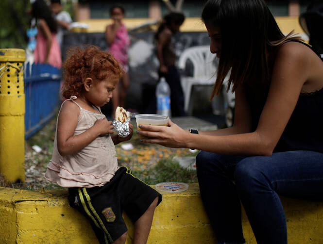 A volunteer with "Make the Difference" charity initiative gives a cup of soup and an "arepa" to a homeless child along a street in Caracas, Venezuela, March 5, 2017. Caracas in recent years has seen tear gas attacks, physical assaults on citizens by government forces, and hungry and malnourished crowds asking for help in streets that once boasted some of the most well-off people in all of Latin America. (CNS photo/Marco Bello, Reuters)