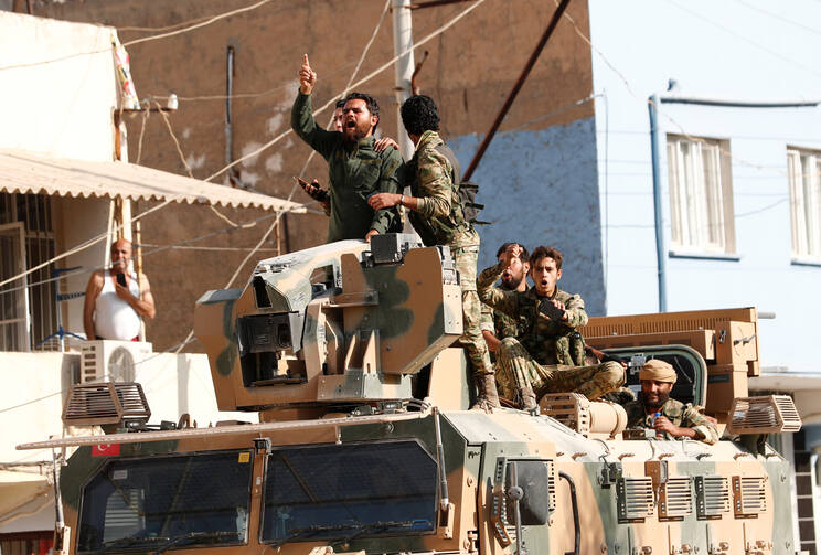 Members of Syrian National Army, known as the Free Syrian Army, react as they drive on top of an armored vehicle Oct. 11, 2019, in the Turkish border town of Ceylanpinar. Dozens of advocacy organizations participating in the International Religious Freedom Roundtable called on U.S. President Donald Trump "not to abandon Christians, Yazidis and Kurds" in the Syrian border region that Turkey is bombing. (CNS photo/Murad Sezer, Reuters)