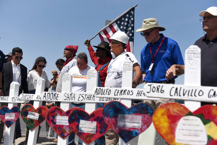 People hold hands in prayer Aug. 5, 2019, next to crosses in honor of victims of a mass shooting at a Walmart store in El Paso, Texas, two days earlier. A year after the deadly shooting, El Paso Bishop Mark J. Seitz has announced the formation of a group to address racism as a way to honor the victims. (CNS photo/Callaghan O'Hare, Reuters)