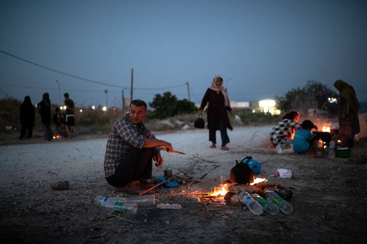 People displaced from the destroyed Moria refugee camp sit by fires along a road on the Greek island of Lesbos Sept. 15, 2020. The camp, which was mostly destroyed in fires Sept. 9, was home to at least 12,000 people, six times its maximum capacity of just over 2,000 asylum-seekers. (CNS photo/Alkis Konstantinidis, Reuters)