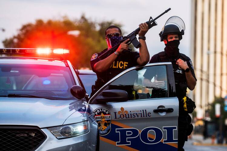 Louisville police officers stand guard on Sept. 26, as demonstrators march during a peaceful protest after a grand jury handed down an indictment on Sept. 23 for one of three police officers involved in the fatal shooting of Breonna Taylor. (CNS photo/Eduardo Munoz, Reuters)