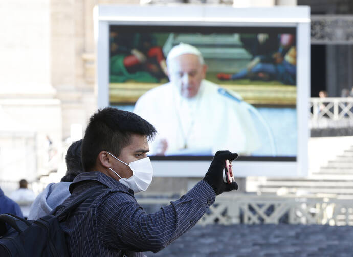 A man wearing a mask takes a photo as Pope Francis appears on a video monitor in St. Peter's Square as he leads the Angelus from his library in the Apostolic Palace at the Vatican March 8, 2020. (CNS photo/Paul Haring)