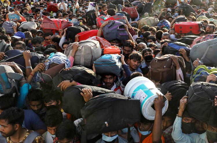 Migrant workers crowd outside a bus station in Ghaziabad, India, March 28, 2020, as they wait to board buses to return to their villages during a 21-day nationwide lockdown to limit the spread of COVID-19. (CNS photo/Anushree Fadnavis, Reuters)