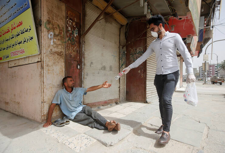 An Iraqi man wearing a protective face mask gives a bottle of water to a homeless man in Basra on April 2. (CNS photo/Essam al-Sudani, Reuters) 