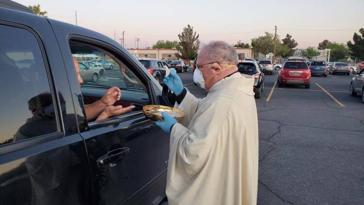 Bishop Peter Baldacchino of Las Cruces, N.M., wears a mask and gloves while giving Communion to a passenger of a vehicle during the Easter Vigil in the parking lot of the Cathedral of the Immaculate Heart of Mary in Las Cruces April 11, 2020. Bishop Baldacchino became the first-known U.S. prelate to lift a diocesan ban on public Mass April 15, 2020, and told priests they may resume sacramental ministry if they follow state health mandates. (CNS photo/courtesy David McNamara, Diocese of Las Cruces)