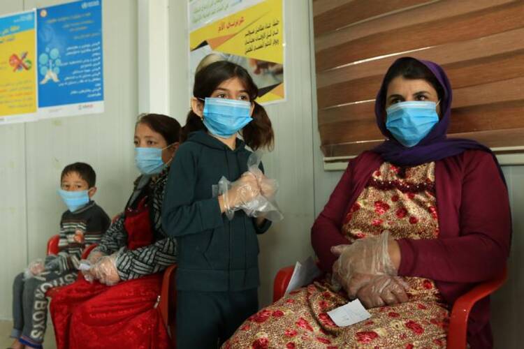 Displaced women and children wearing protective masks wait in the medical center of a camp in Dahuk, Iraq, March 7, 2020, during the COVID-19 pandemic. (CNS photo/Ari Jalal, Reuters)