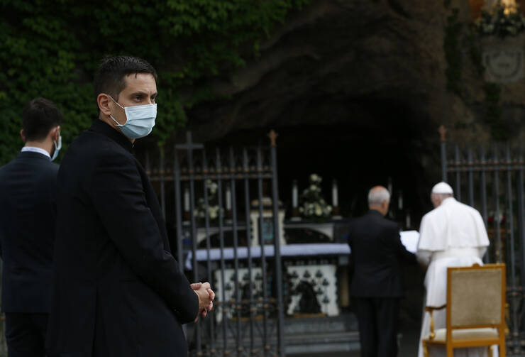 A cleric wears a mask as Pope Francis leads the recitation of the rosary during a prayer service at the Lourdes grotto in the Vatican Gardens on May 30. (CNS photo/Paul Haring) 