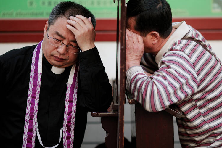 A file photo shows a priest hearing confession at the Cathedral of the Immaculate Conception in Beijing. The Chinese government said that in addition to meeting health requirements after the COVID-19 outbreak, priests must "preach on patriotism" as a condition for reopening their churches. (CNS photo/Damir Sagolj, Reuters) 