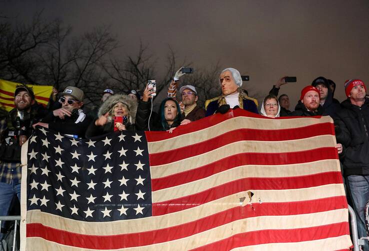 People without masks hold an American flag next to a bust of George Washington doing the same