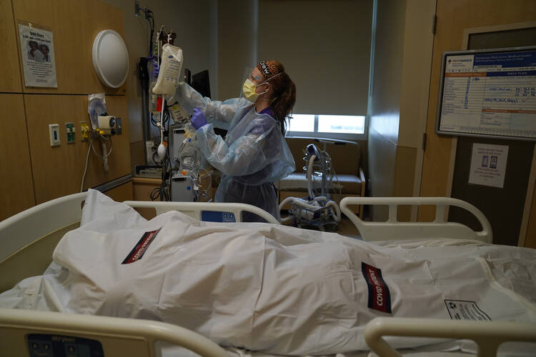 Registered nurse Nikki Hollinger cleans up a room as a body of a COVID-19 victim lies in a body bag labeled with stickers at Providence Holy Cross Medical Center in the Mission Hills section of Los Angeles, Saturday, Jan. 9, 2021. The U.S. death toll from the coronavirus has eclipsed 400,000 in the waning hours in office for President Donald Trump. (AP Photo/Jae C. Hong)