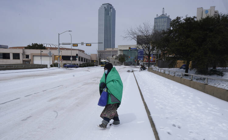 A woman wrapped in a blanket crosses the street near downtown Dallas, Tuesday, Feb. 16, 2021. Temperatures dropped into the single digits as snow shut down air travel and grocery stores. (AP Photo/LM Otero)