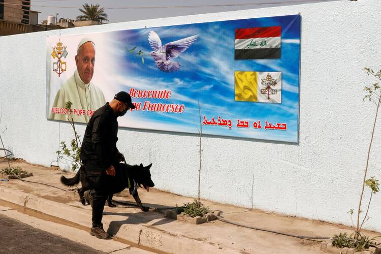 A security officer walks with a K-9 unit dog near a poster of Pope Francis in Baghdad on March 3, 2021. (CNS photo/Khalid al-Mousily, Reuters)