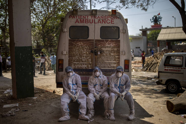 Exhausted workers, who bring dead bodies for cremation, sit on the rear step of an ambulance inside a crematorium, in New Delhi, India, on April 24. Delhi has been cremating so many bodies of coronavirus victims that authorities are getting requests to start cutting down trees in city parks, as a second record surge has brought India's tattered healthcare system to its knees. (AP Photo/Altaf Qadri)